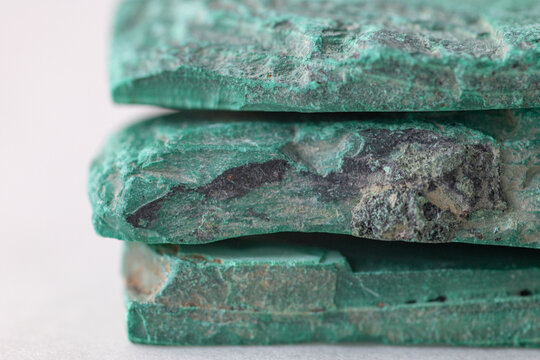 Raw malachite mineral slabs stacked on white surface, flat sliced stone pieces with rough edges and green layered structure, natural pigment source material.