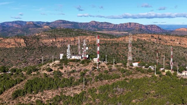 Rising orbit aerial footage of a mountain telecommunications site with multiple lattice towers, microwave links and support buildings, demonstrating high-altitude broadcast and wireless infrastructure