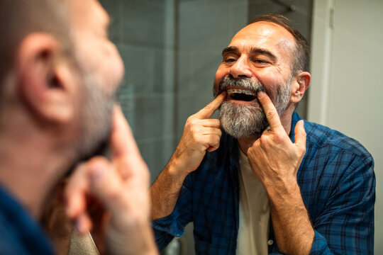 Middle-aged man showing braces in bathroom mirror