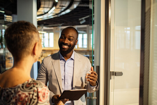 Smiling businessman greeting coworker with tablet in modern office