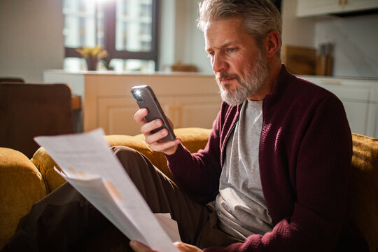 Mature man scanning bills with smartphone at home