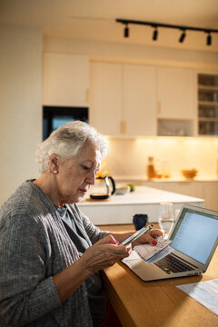 Senior woman paying bills with smartphone in home kitchen