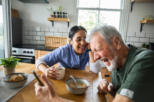Caregiver and senior man laughing over breakfast at home