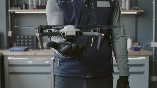 Technician holding modern drone inside workshop. Professional checking equipment before flight. Concept of technology, industrial maintenance and robotics innovation.