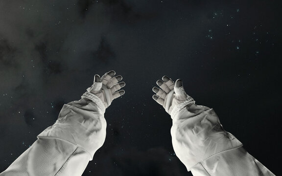 A close-up, first-person view of astronaut hands reaching out into the cold, dark expanse of outer space, with distant stars visible