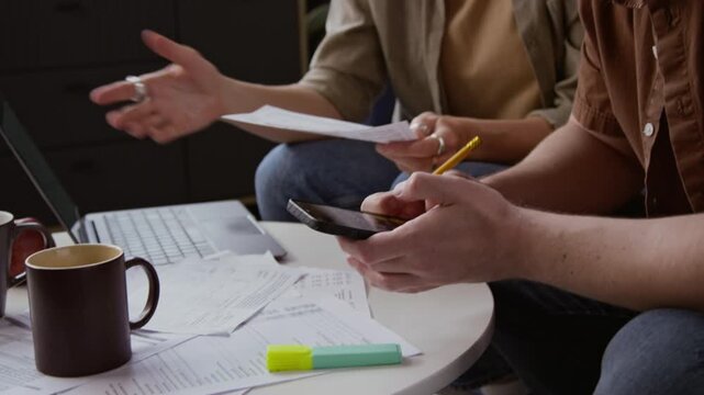 Side view close up shot of adult couple planning home finances and doing budgeting together with focus on hands holding bills with past due notice, copy space