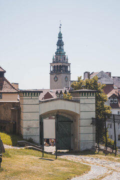View of the historic entrance gate leading to the town center of Kłodzko. The Neo-Renaissance tower of the Town Hall (Ratusz) is visible in the background against a clear blue sky.