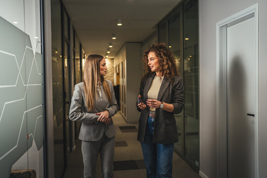 Businesswomen walking and conversing in modern office corridor
