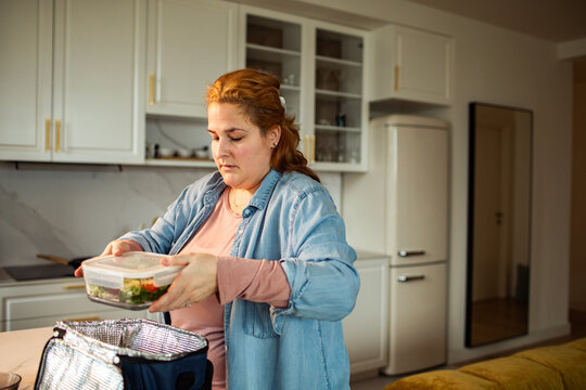 Woman packing healthy lunch into insulated bag in home kitchen