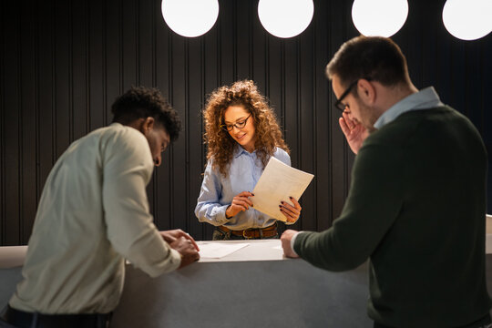 Receptionist assisting diverse clients with paperwork at office desk