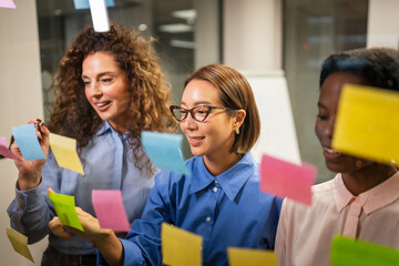 Diverse businesswomen brainstorming creative ideas on glass wall