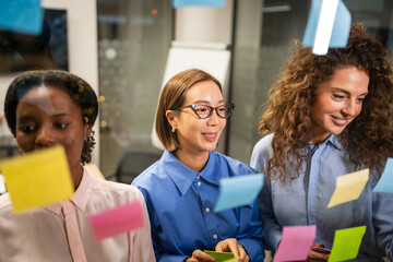 Diverse businesswomen brainstorming creative ideas on glass wall