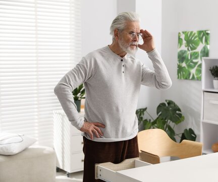 Amnesia. Senior man trying to remember something at white table indoors