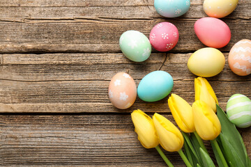 Obraz premium Painted Easter eggs and beautiful tulips on wooden table, flat lay. Space for text