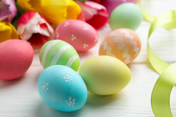 Obraz premium Painted Easter eggs, beautiful tulips and ribbon on white wooden table, closeup