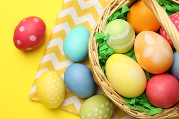 Obraz premium Easter basket with painted eggs on yellow background, flat lay