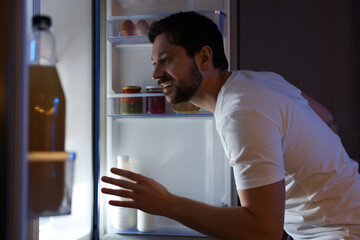 Man looking into open refrigerator in kitchen
