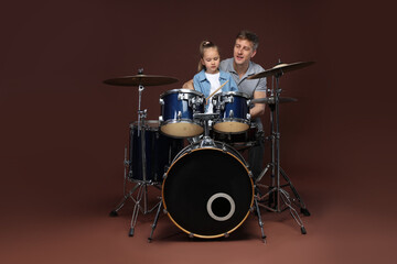 Little girl learning how to play drums with music teacher on brown background