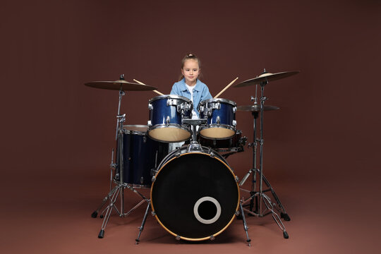 Little girl learning how to play drums on brown background