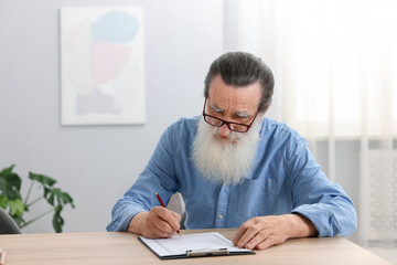 Senior man signing Last Will and Testament at wooden desk indoors, space for text