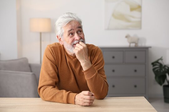 Amnesia. Senior man trying to remember something at wooden table indoors, space for text