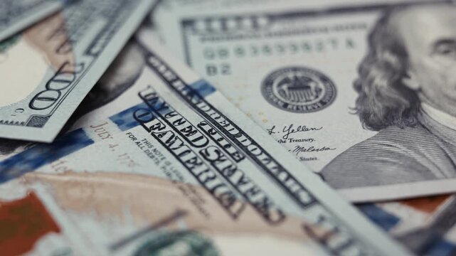 Close-up view of assorted United States currency bills stacked together, showcasing intricate designs and details of hundred-dollar notes on a flat surface