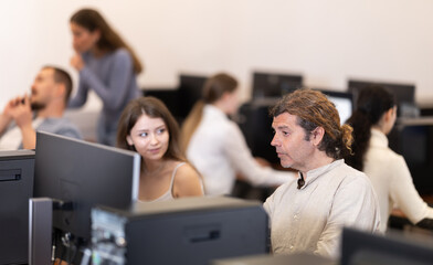 Fototapeta premium Adult man working on computer and talking to young woman colleague in office
