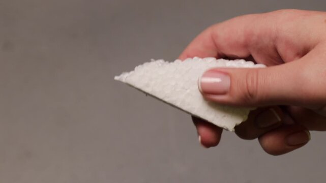 Closeup of a person hand holding and rubbing a textured piece of styrofoam, capturing the tactile experience and sound associated with the material