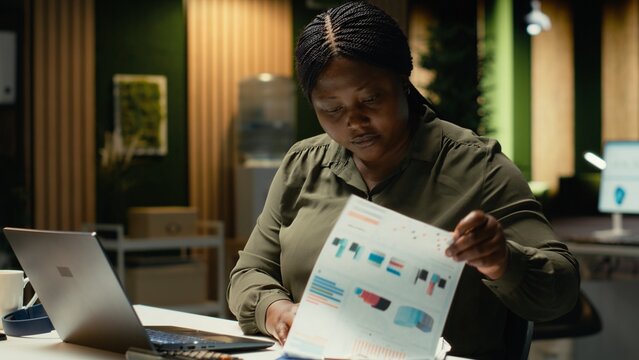 Female employee researching and documenting data reports numbers for data updates and business enterprise, after hours work in dark office. Finance targets and project development. Camera B.
