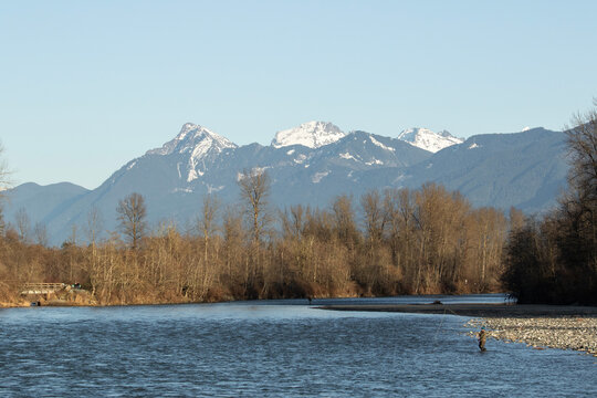Angler fishing in the Chilliwack river in a sunny winter day with the mountains in the background.