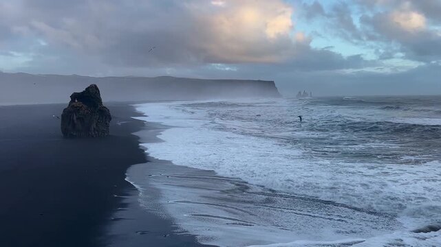 Wide angle static shot of Reynisfjara black sand beach and Reynisdrangar basalt sea stacks from Dyrholaey cliffs, South Iceland.