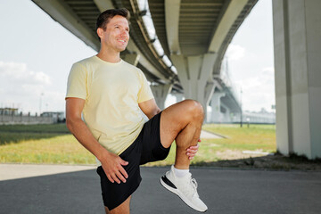Obraz premium Man stretches his leg under a bridge before running in an outdoor area during daytime