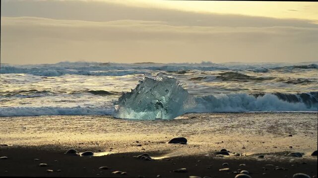 Static shot of a large ice diamond on black sand beach with crashing waves at sunset, Diamond Beach, Iceland. HD 1080p.