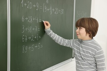 Schoolboy doing math on chalkboard in classroom