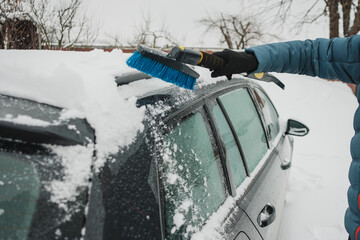 Person brushing snow from car roof after snowfall