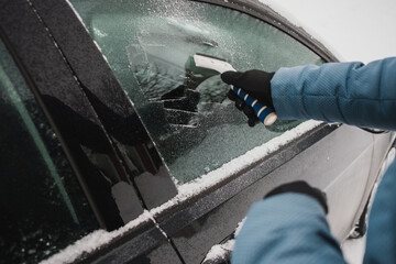 Person scraping ice off car window during winter