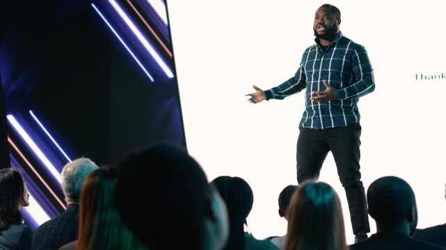 African american lead engineer revealing new smartphone launch with detailed presentation about new interface features for advertising. Launch with audience in conference hall. Camera B.