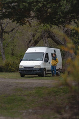 Man standing next to a white camper van in a wooded area
