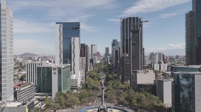 Aerial drone flying forward past &Aacute;ngel de la Independencia revealing Paseo de la Reforma skyline with blue sky in M&eacute;xico City