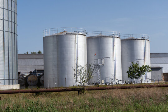 Storage Silos Stand in a Field Near a Building Under Clear Sky During Daylight Hours