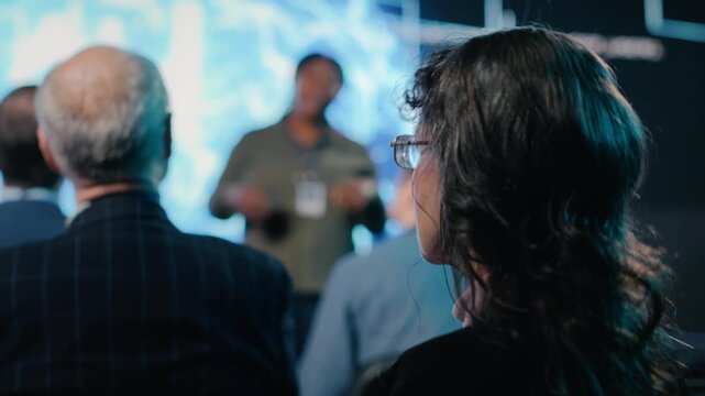 Senior female in the audience listening to AI sales pitch featuring neural networks, AI brain machine learning. Entrepreneur speaker explains funding and investment deal opportunities. Camera B.