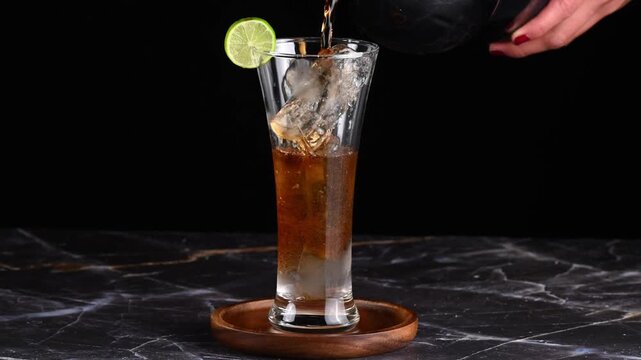 Cuba libre drink, Close-up of cola being poured into a glass with ice cubes, slow motion
