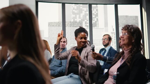 African american woman interacting and sharing opinion on microphone during panel discussion. Diverse group of colleagues and participants attend international business summit. Camera A.