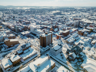 Fototapeta premium High angle aerial view of a city covered in deep white snow under a bright clear blue sky.