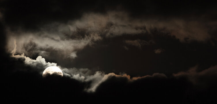 Bright full moon peeking through heavy clouds