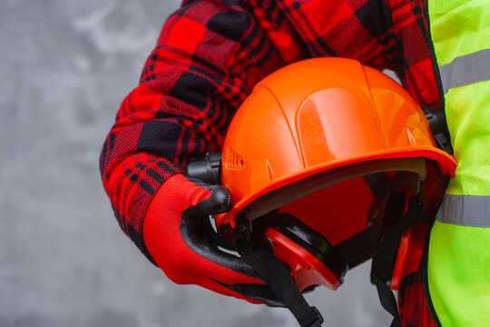Professional construction worker is holding a safety helmet with earmuffs. The emphasis is on workplace safety PPE, health protection and professional equipment.