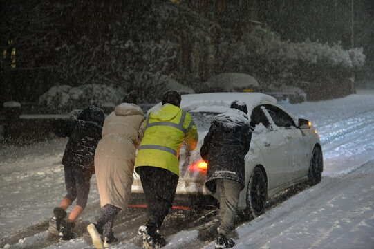 Heavy snowfall blocking the roads caused cars to become stuck on the ice in Hertford, England, UK.  People pushing a car up a slippery hill. The hill is located leaving the town via the A414.