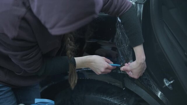 Professional detailer installing Paint Protection Film (PPF) on car B-pillar. Close-up of hands using squeegee and knife to apply transparent anti-gravel vinyl.