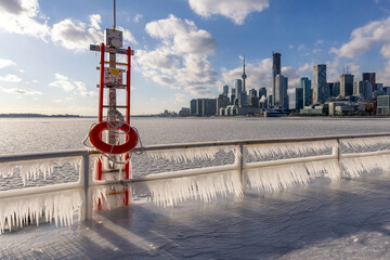 Naklejka premium Icicles forming on a rail at a frozen pier - Toronto skyline in the background from Polson Pier