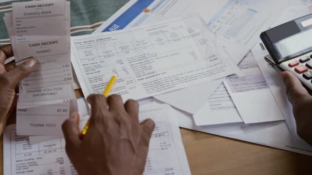 Close up shot of hands holding calculator and pointing at bills and receipts while family managing home finances together